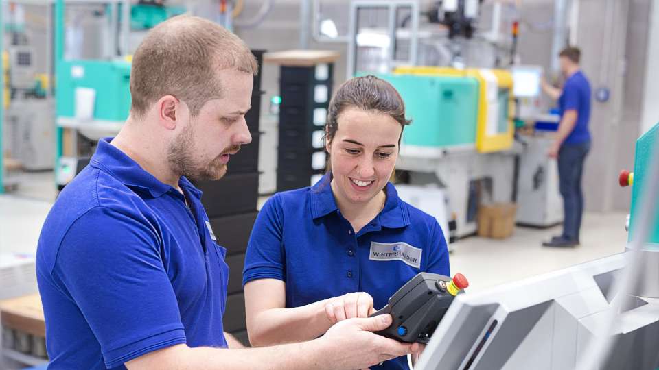 Zwei Mitarbeitende arbeiten an Spritzgussmaschine